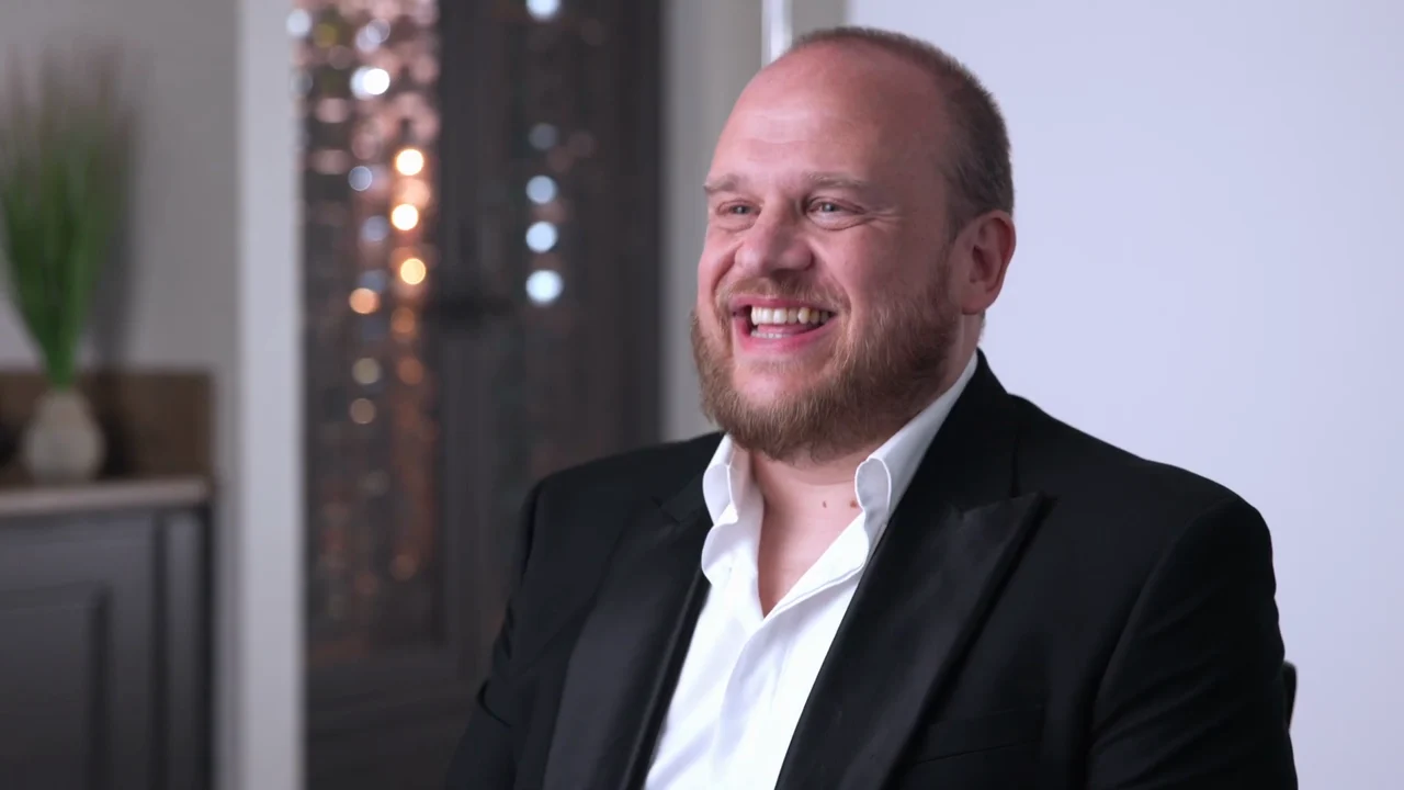 Wide interview setup with James Kay seated against a white backdrop